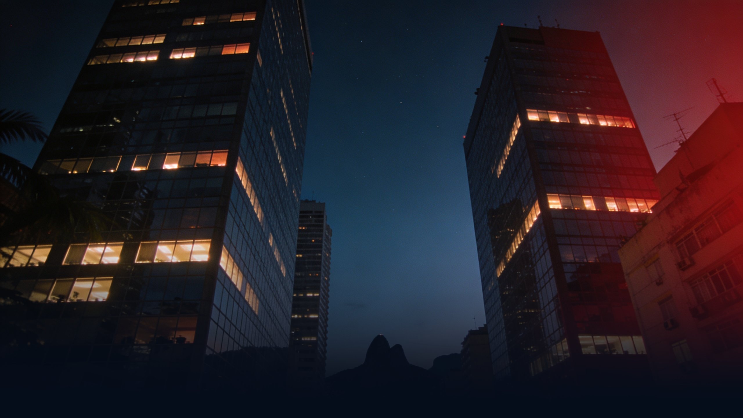 Rio de Janeiro skyline at blue hour photographed from a low ground angle, modern corporate glass towers in the Centro district with backlit windows glowing warm tungsten against deep navy tropical twilight sky