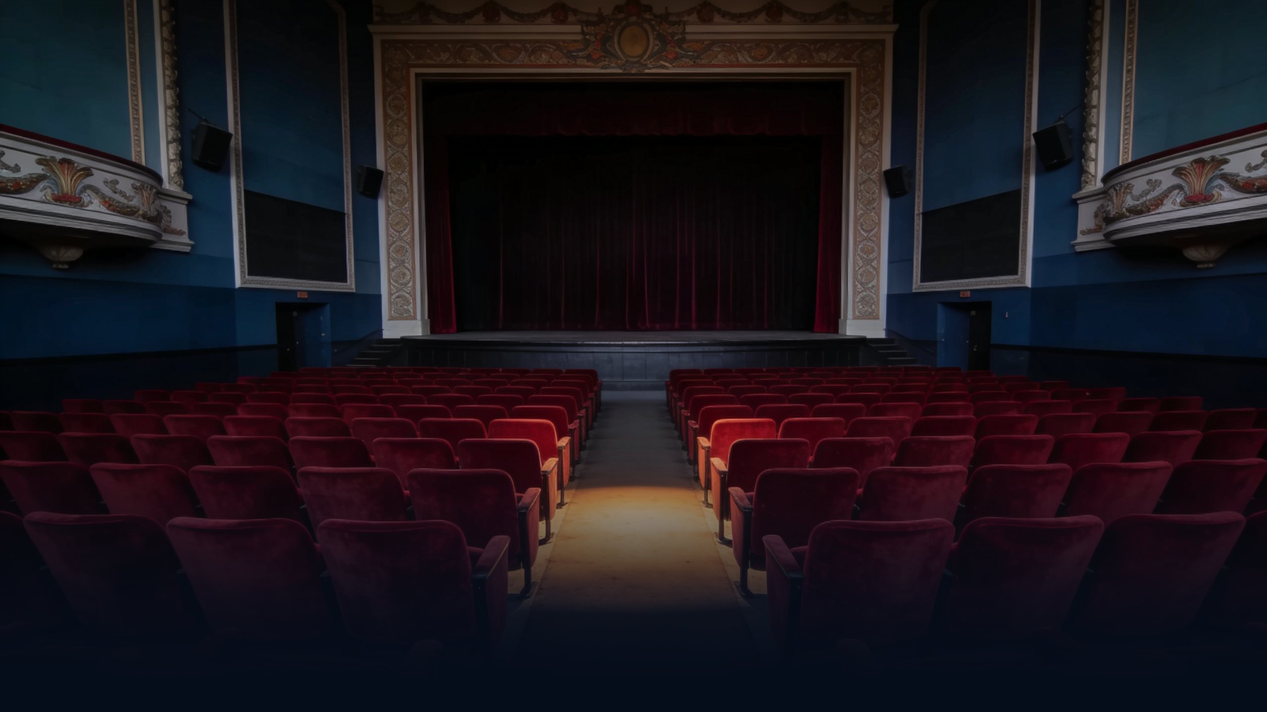 Empty classic American single-screen movie theater interior at twilight, ornate molding, rows of red velvet seats facing a dark curtained screen
