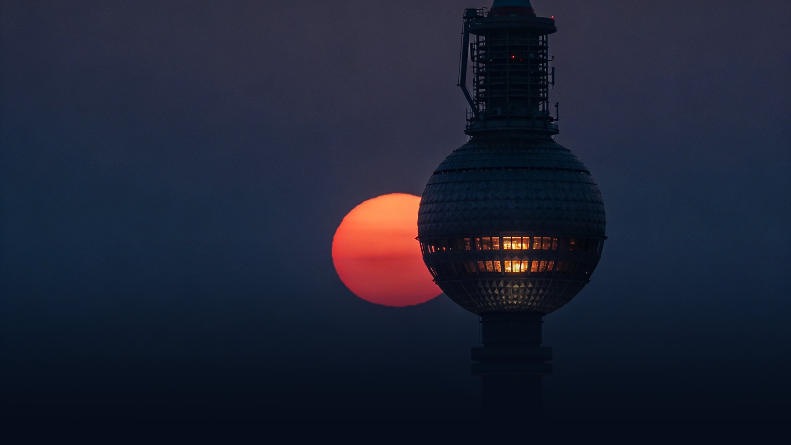 Berlin Fernsehturm TV tower silhouetted against deep navy twilight sky from a distance, telephoto compression, sphere catching last warm light of sunset